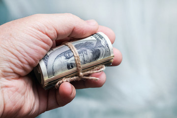 A man holds  in his hand Money (US dollars) in a roll tied with a rope
