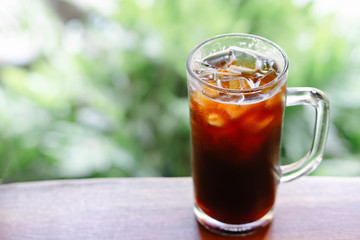 Closeup glass of ice americano coffee on wood table with green nature background, selective focus