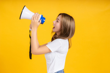 Speaking Loud noise announce of young asian woman with megaphone promotional advertising in white t-shirt smiling emotion on yellow background isolated studio shot with copy space.