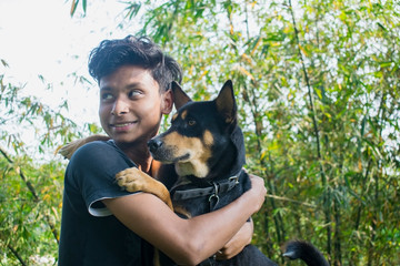 a teenager boy with his pet indian black dog outdoor in front of natural background