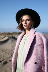 Vertical image of good looking female model posing on nature wearing pink coat and fedora hat. Outdoor.