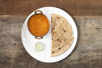 Handmade flat bread chapati and dal tadka fry in brass bowl pan on white plate rustic wooden background