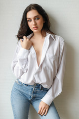 portrait of seated young woman wearing a bouffant shirt with naked shoulders on light grey background. Beautiful brunette girl in jeans and white t-shirt smiling