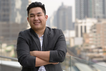 Happy young overweight Asian businessman smiling with arms crossed - 338806732