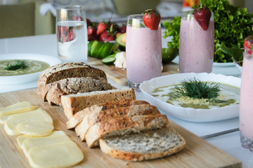 Strawberry smoothie, broccoli soup, fresh vegetables and berries, cheese and bread on wooden board on white background.