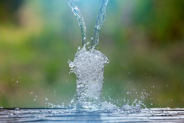 Naklejka na ściany i meble Drink water pouring in to glass over sunlight and natural green background.Select focus blurred background.Fersh Clean water splash.