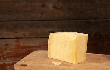 slice of hard Parmesan cheese lies on a wooden board, brown background