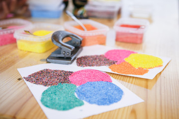 Creative items and crafts for children at home on the table. Paints and brushes, scissors, thread and scraps of fabric - the hands of the child and the parent in the background.