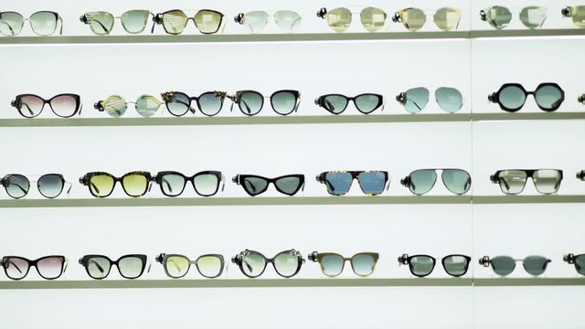 fashion boutique stand, various modern designer sunglasses lying on shelves in white background closeup, circling camera motion