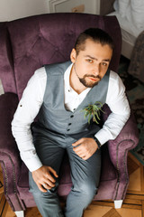 A serious boy in a gray suit sits on a soft chair in the room