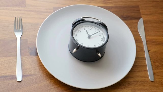 The alarm clock lies on an empty plate, kurpny plan. Concept: cooking, diet, diet, healthy food, hunger, appetite, fitness, hunger