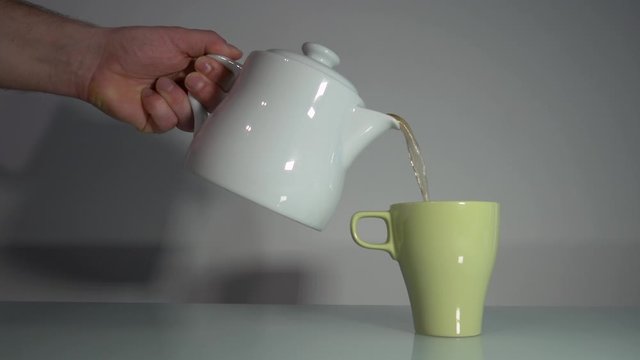 Pouring Hot Tea From A White Teapot To A Light Green Cup During Tea Time - Closeup Shot