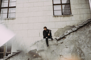 Emotional portrait of a guy on the ruins. Emotions, depression, stress. Frame from the movies. disc cover. book cover. sitting on the steps of an old building