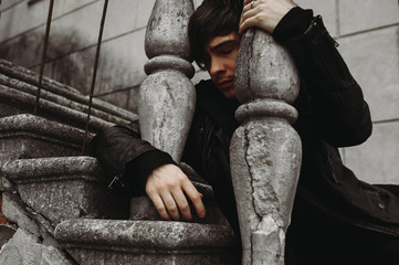 Emotional portrait of a guy on the ruins. Emotions, depression, stress. Frame from the movies. disc cover. book cover. sitting on the steps of an old building