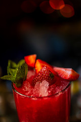 A refreshing red cocktail decorated with a strawberry and mint on the bar counter. Close-up, a dark background