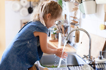 Kid washing hands at home under water tap. Cute child girl in flour after cooking in cozy kitchen....