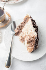Slice of Tiramassu cake on a white plate. Home made. Near a fork and a cup of coffee. Top view White background.