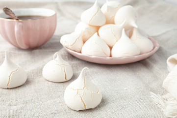 Meringue cookies with texture and cracks in the foreground. In the background, the meringues lie on a pink plate. Gray linen background. Close-up.