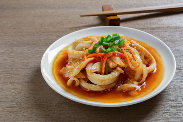 close up of stir fried squid with kimchi in a ceramic dish on wooden table. homemade style food concept.