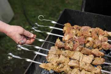 Pork shashlik kebab is fried on the grill on coals on skewers with a man hand on the dacha. Background image, copy space