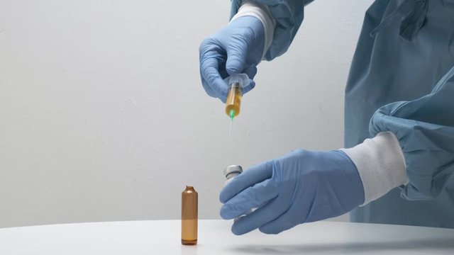 closeup on man's hands filling glass vial with powder with solution from syringe. doctor preparing injection for patient from vaccine bottle. Medicine, healthcare, medical concept, clinic vaccination