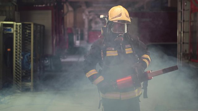 firefighter portrait wearing full equipment, oxygen mask, and power hydraulic cutting tool, smoke and fire trucks in the background. Name tag translation is fireman and model's last name.

