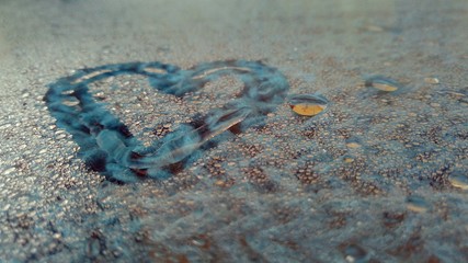 heart painted on wet glass and against a background of blue knitted material in a creative photo