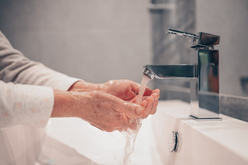 Hand washing lather liquid soap rubbing wrists handwash step senior woman rinsing in water at bathroom faucet sink. Wash hands for COVID-19 spreading prevention. Coronavirus pandemic outbreak.