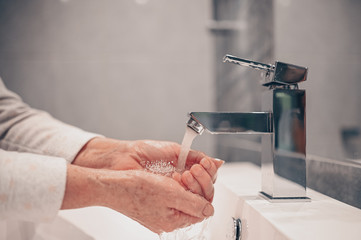 Hand washing lather liquid soap rubbing wrists handwash step senior woman rinsing in water at bathroom faucet sink. Wash hands for COVID-19 spreading prevention. Coronavirus pandemic outbreak.