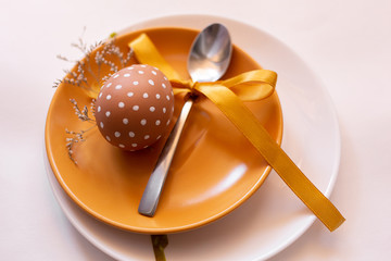 Painted brown egg with various white patterns for Easter holiday on yellow and white plate with herbs. Spoon with yellow ribbon. Traditional for Eastern European cultures. Top view