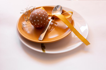 Painted brown egg with various white patterns for Easter holiday on yellow and white plate with herbs. Spoon with yellow ribbon. Traditional for Eastern European cultures. Top view