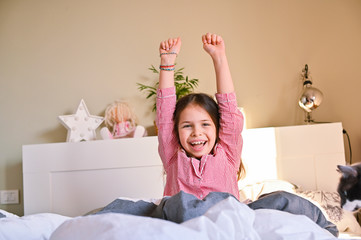 The little girl woke up. The child in his pajamas stretches in bed, smiling shows positive...
