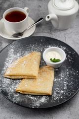 Plain thin crepes with butter and sour cream with a cup of tea and a teapot