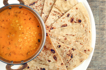 Handmade flat bread chapati and dal tadka fry in brass bowl pan on white plate rustic wooden background
