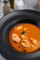 Hot and spicy tomato seafood soup with salmon, prawns and squids, close up