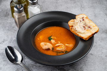 Hot and spicy tomato seafood soup with salmon, prawns and squids, close up