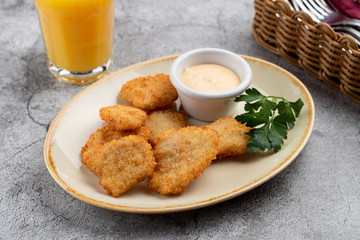 Breaded crispy chicken nuggets with cheese sauce on grey table, served with orange juice