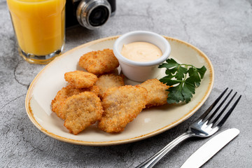 Breaded crispy chicken nuggets with cheese sauce on grey table, served with orange juice