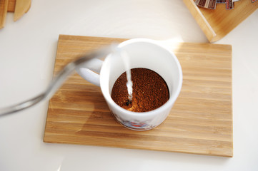 Brewing coffee in mug. Pouring water from gooseneck kettle into cup with freshly ground coffee top view
