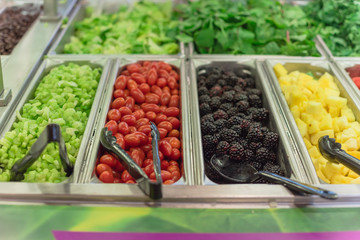 Cherry tomatoes, blackberries, pineapple chunks, strawberry, red grape trays at salad bar in USA