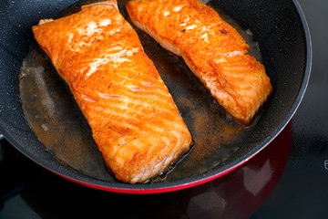 Salmon fillets in frying pan cooking on induction hob.