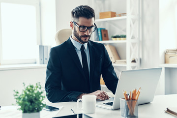 Confident young man in elegant business suit working using lapto