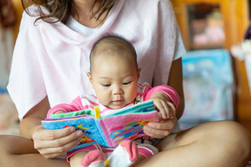 6-month-old Asian girl sat on the mother's lap and reading a children's story book.
