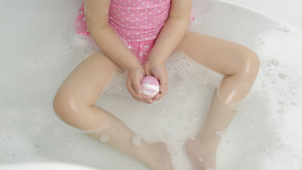 Hands of girl puts bath bomb to water. Ball of bath salt dissolves in water