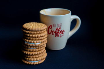 A pile of cookies and a coffee cup on dark black background, side view