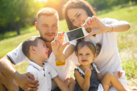 Happy family making selfie on smartphone. Happy people resting together with their children outdoors.
