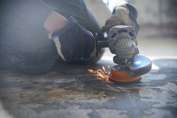 A man in gloves and protective knee pads on the legs grinds the floor with a grinder