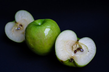 One whole green sour apple and two halves of the apple on dark black background