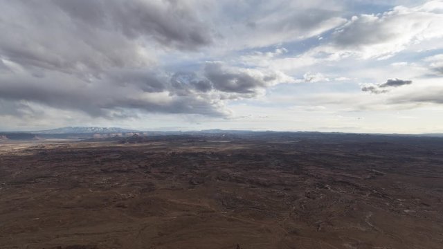 An ultra-wide timelapse looking across Canyonlands National Park and the distant Abajo Mountains as seen from Needles Overlook. Clouds clear overhead revealing blue skies in the distance.