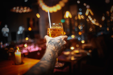 tattooed male hand holding cocktail in restaurant